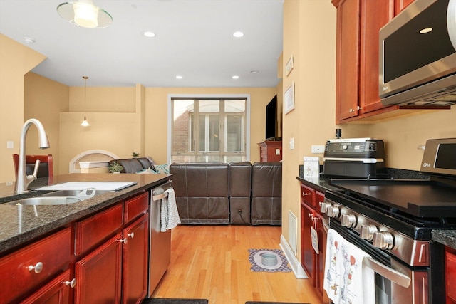 kitchen featuring pendant lighting, appliances with stainless steel finishes, light wood-type flooring, dark brown cabinets, and a sink