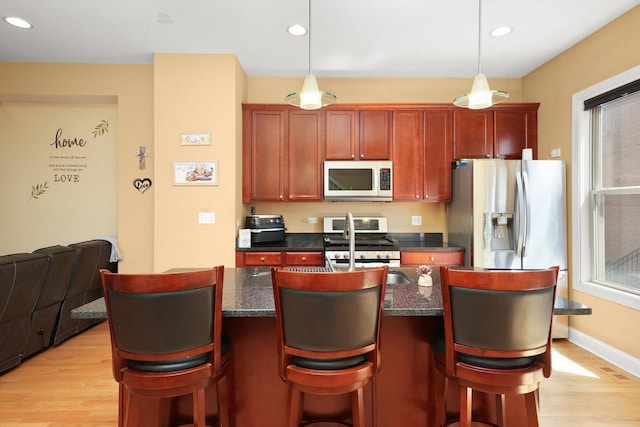kitchen featuring a kitchen island with sink, visible vents, appliances with stainless steel finishes, hanging light fixtures, and light wood-style flooring