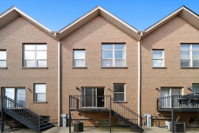 rear view of house featuring brick siding, central AC unit, and stairs