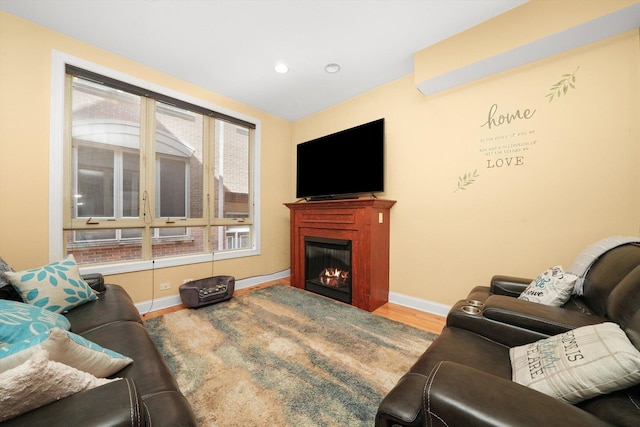 living area featuring baseboards, a lit fireplace, recessed lighting, and wood finished floors