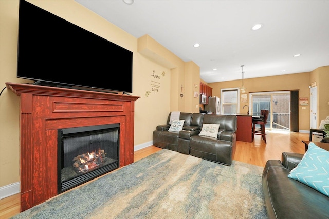 living area with recessed lighting, baseboards, a lit fireplace, and light wood-style floors