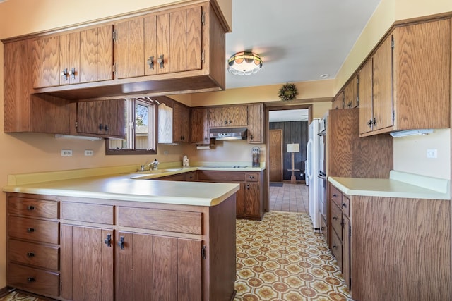kitchen featuring a peninsula, under cabinet range hood, light countertops, and brown cabinets