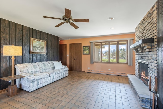 living area featuring a brick fireplace, ceiling fan, baseboard heating, wood walls, and tile patterned floors