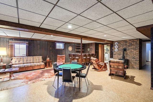 rec room with wood walls, a wood stove, plenty of natural light, and a drop ceiling