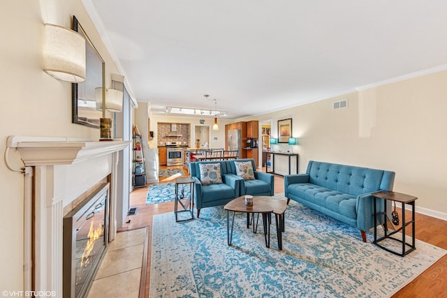 living room with a glass covered fireplace, baseboards, light wood-type flooring, ornamental molding, and visible vents