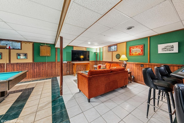 tiled living area featuring wood walls, visible vents, a paneled ceiling, and a wainscoted wall