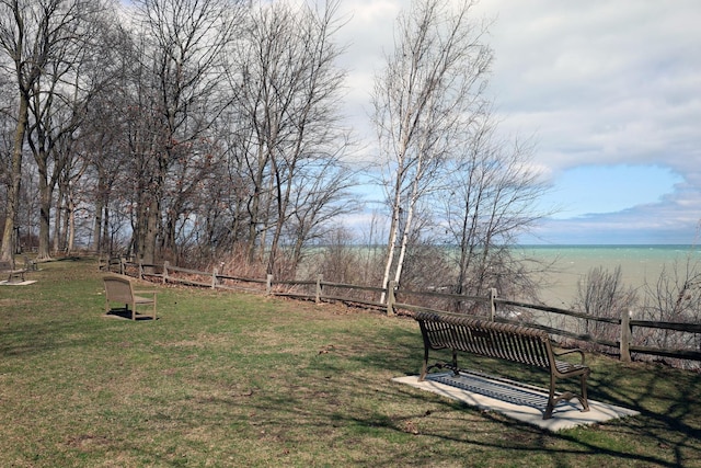 surrounding community featuring fence, a water view, and a lawn
