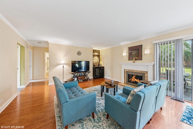 living area featuring a glass covered fireplace, baseboards, crown molding, visible vents, and wood finished floors