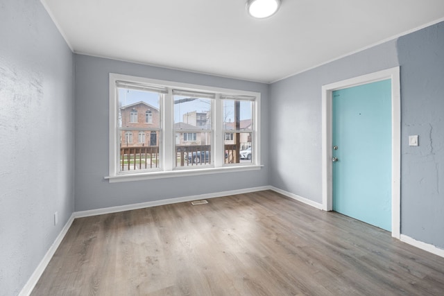 unfurnished room featuring wood finished floors, baseboards, ornamental molding, and visible vents