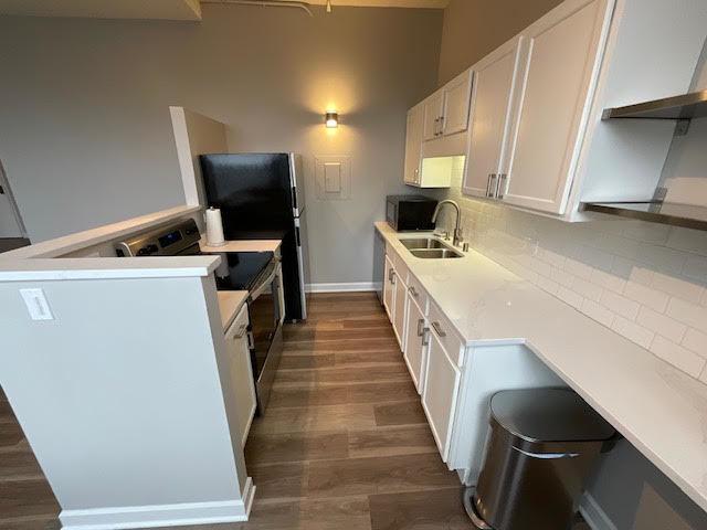 kitchen featuring appliances with stainless steel finishes, a sink, dark wood finished floors, white cabinetry, and light countertops