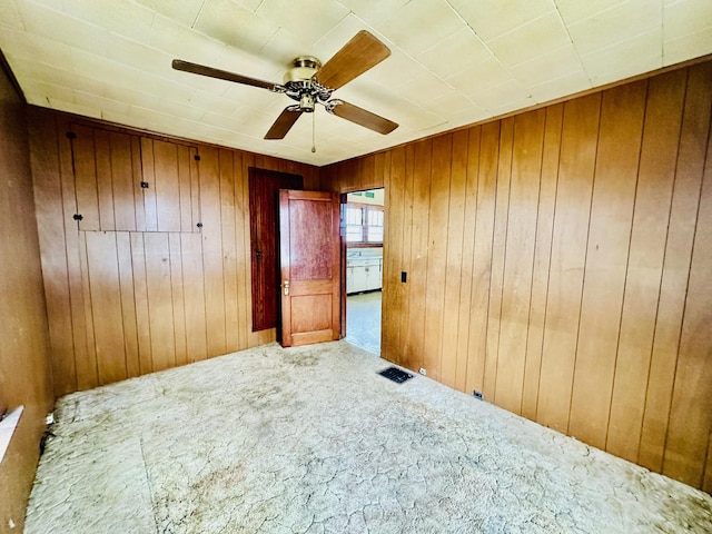carpeted spare room featuring visible vents, a ceiling fan, and wood walls