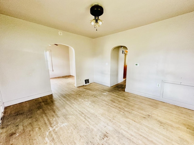 spare room with baseboards, visible vents, ceiling fan, arched walkways, and wood finished floors