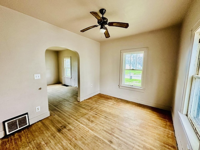 spare room featuring baseboards, a ceiling fan, visible vents, arched walkways, and wood finished floors