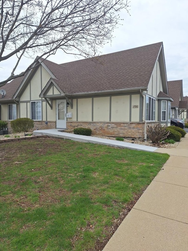 tudor home featuring a shingled roof, stucco siding, a front lawn, and brick siding