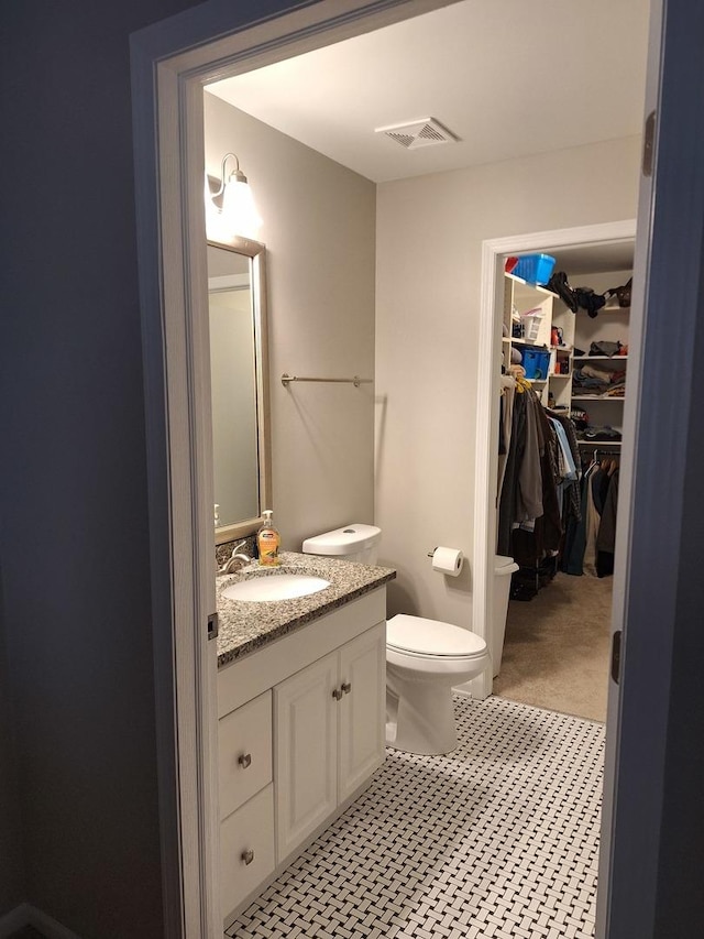 bathroom with visible vents, toilet, a walk in closet, and vanity