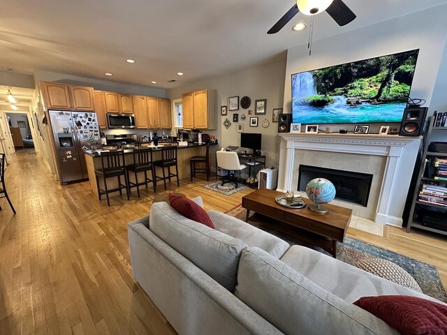living area featuring a ceiling fan, recessed lighting, a tile fireplace, and light wood-style floors