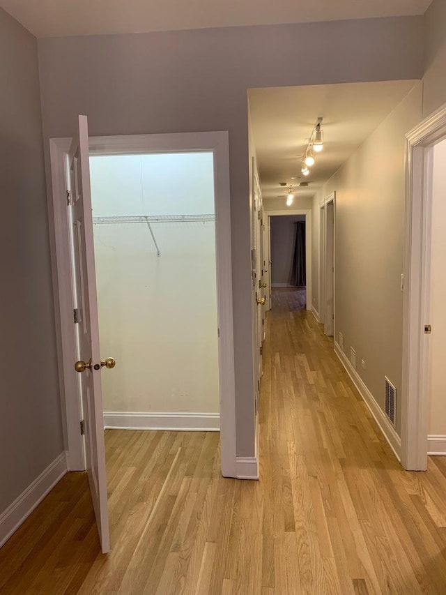 hallway with track lighting, baseboards, light wood-type flooring, and visible vents