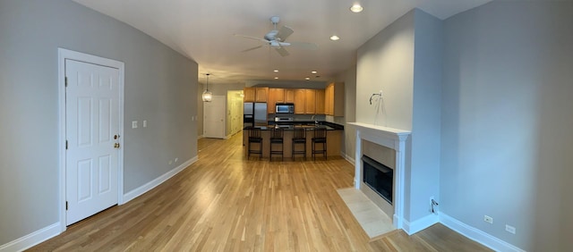living room featuring ceiling fan, a fireplace with flush hearth, baseboards, and light wood-style floors