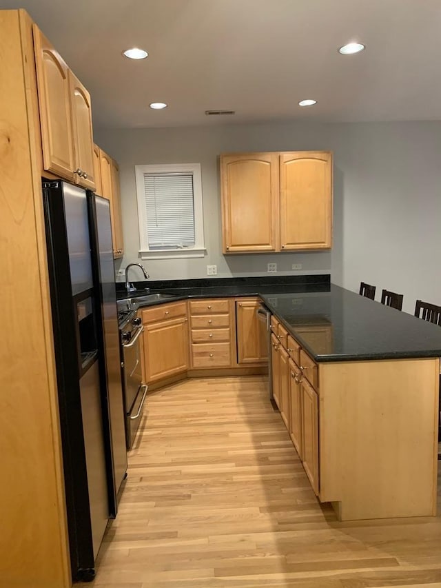 kitchen featuring light brown cabinetry, light wood-style floors, a peninsula, fridge with ice dispenser, and gas range