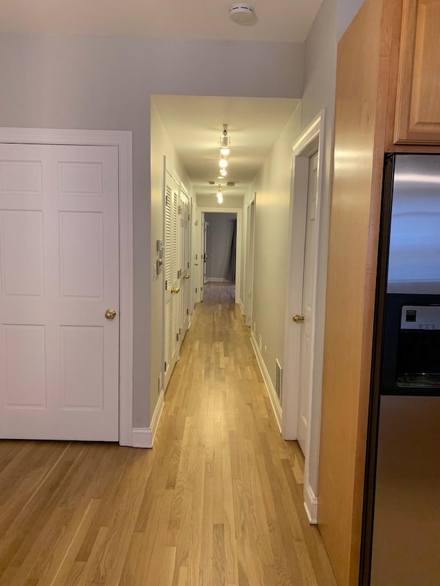 hall featuring light wood-style floors, baseboards, and visible vents
