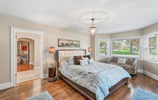 bedroom with arched walkways, baseboards, a notable chandelier, and wood finished floors
