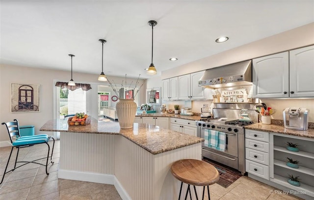 kitchen featuring wall chimney range hood, stainless steel range with gas stovetop, a breakfast bar, and light stone countertops