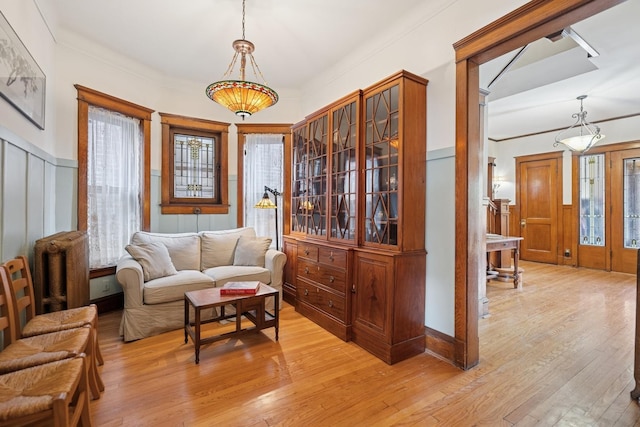 sitting room featuring light wood-type flooring, crown molding, and a wainscoted wall