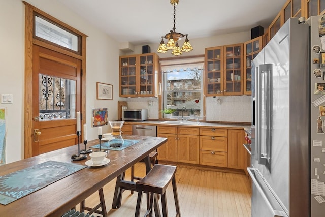kitchen with appliances with stainless steel finishes, a sink, glass insert cabinets, and a notable chandelier