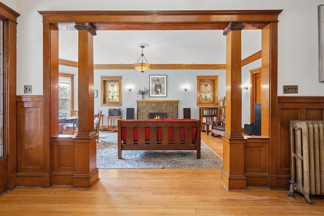 interior space with radiator, light wood finished floors, a warm lit fireplace, and a wainscoted wall