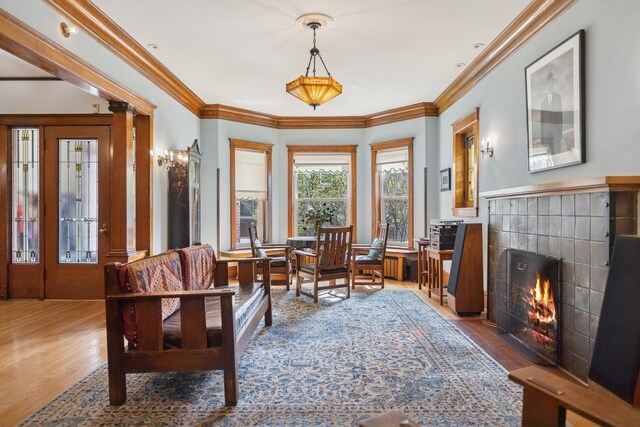 living area with ornamental molding, a tile fireplace, and wood finished floors