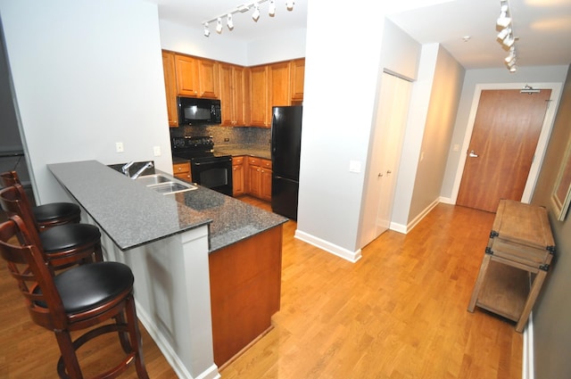 kitchen featuring tasteful backsplash, a peninsula, light wood-type flooring, black appliances, and a sink