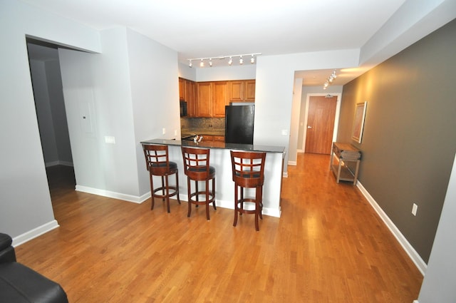 kitchen featuring dark countertops, backsplash, freestanding refrigerator, and light wood finished floors
