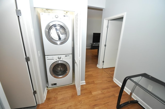 clothes washing area featuring baseboards, light wood finished floors, stacked washer and dryer, and laundry area