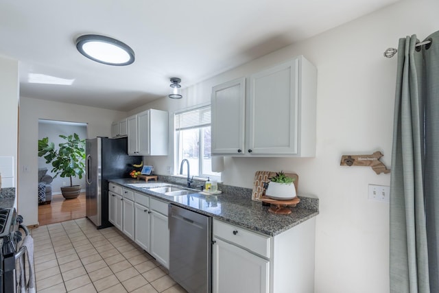 kitchen featuring light tile patterned floors, white cabinets, dark stone counters, stainless steel appliances, and a sink