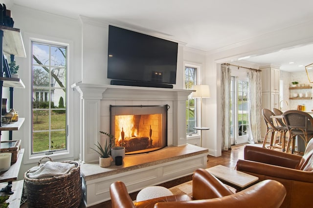 living room with a wealth of natural light, a tiled fireplace, light wood-style flooring, and crown molding