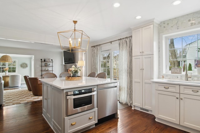 kitchen with a healthy amount of sunlight, appliances with stainless steel finishes, dark wood-style flooring, a sink, and a notable chandelier