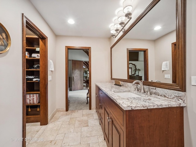 bathroom featuring vanity, baseboards, stone tile flooring, and recessed lighting