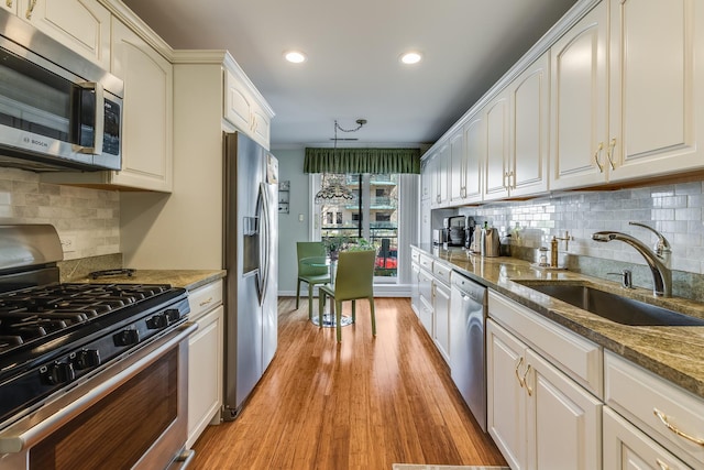 kitchen with tasteful backsplash, a sink, dark stone counters, stainless steel appliances, and light wood-style flooring