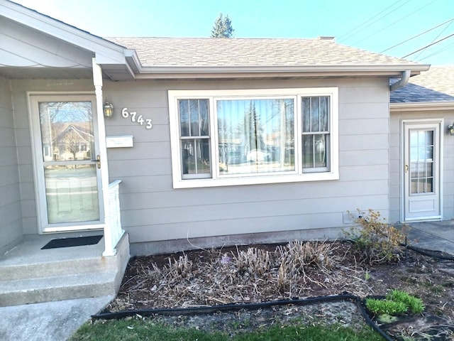 view of exterior entry with roof with shingles