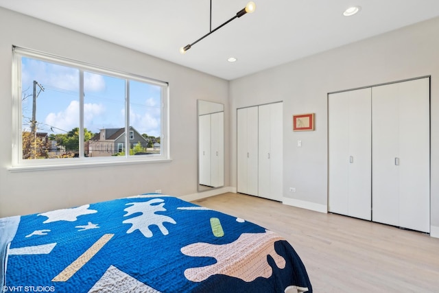 bedroom featuring recessed lighting, light wood finished floors, baseboards, and two closets