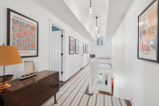 corridor with baseboards, an upstairs landing, vaulted ceiling, and wood finished floors