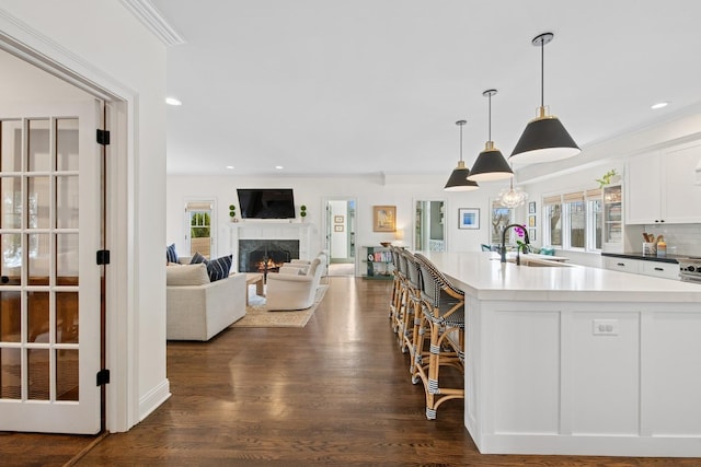 kitchen featuring white cabinetry, a kitchen island with sink, dark wood finished floors, a sink, and a premium fireplace