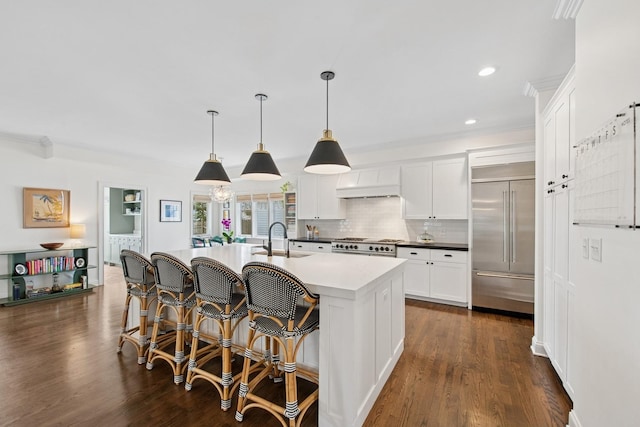 kitchen featuring tasteful backsplash, a sink, a kitchen island with sink, built in fridge, and dark wood finished floors
