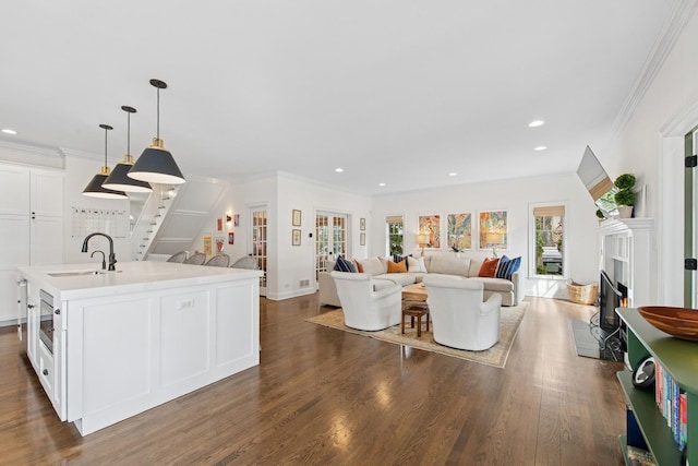 living room featuring a glass covered fireplace, dark wood-style flooring, baseboards, ornamental molding, and recessed lighting