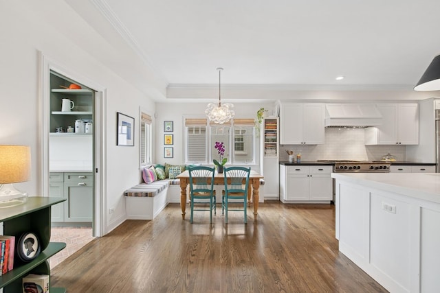 kitchen with crown molding, dark wood-type flooring, white cabinetry, custom exhaust hood, and decorative light fixtures
