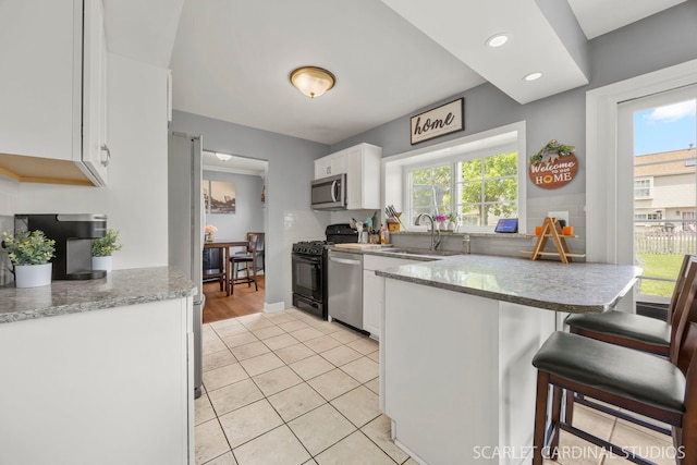 2690 Moss Ln, Aurora, IL 60504 - kitchen featuring appliances with stainless steel finishes, a sink, white cabinets, a peninsula, and light stone countertops