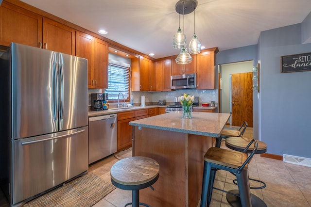 kitchen with appliances with stainless steel finishes, a sink, tasteful backsplash, light tile patterned floors, and a kitchen bar