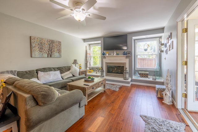 living area with a ceiling fan, a glass covered fireplace, and hardwood / wood-style floors