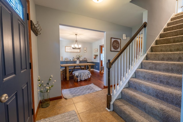 tiled foyer featuring stairs, baseboards, and a chandelier