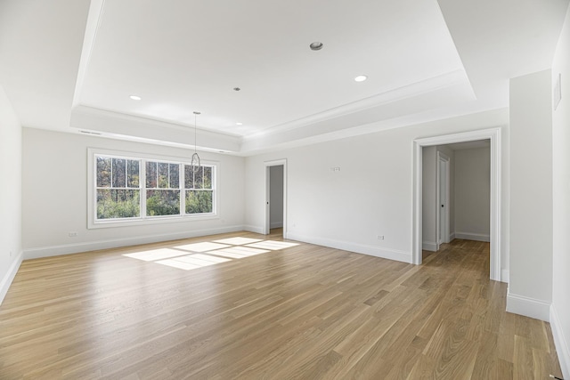 unfurnished living room featuring crown molding, baseboards, a raised ceiling, and light wood-style floors